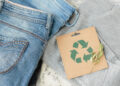 Sustainable still life with Blue denim jeans, gray pullover and craft paper card with Recycling symbol. Second hand apparel idea. Circular fashion, donation, charity concept. Top view