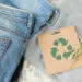 Sustainable still life with Blue denim jeans, gray pullover and craft paper card with Recycling symbol. Second hand apparel idea. Circular fashion, donation, charity concept. Top view
